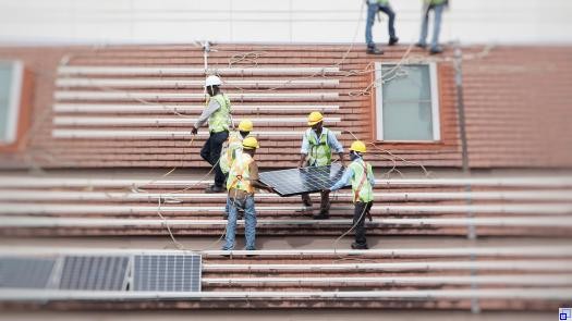 Mehrere Menschen installieren Solarpaneele auf einem Dach