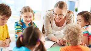 Erzieherin sitzt am Tisch mit einer Gruppe Kinder
