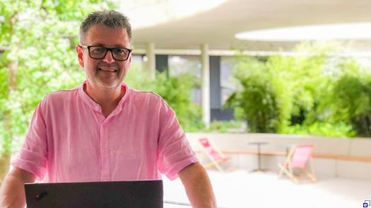 Peter Speicher steht hinter einem geöffneten Notebook, im Hintergrund begrünter Innenhof.