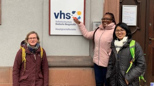 Drei Frauen unterschiedlicher Ethnien stehen vor der Fassade der VHS in Weinheim.