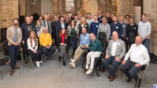 Eine Gruppe Menschen sitzt und steht in den Räumlichkeiten einer ehemaligen Kirche im Halbkreis.
