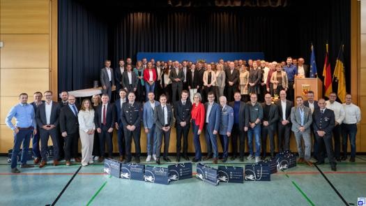 Eine große Gruppe von Menschen in Businesskleidung steht in einer Sport- und Kulturhalle und lächelt in die Kamera.