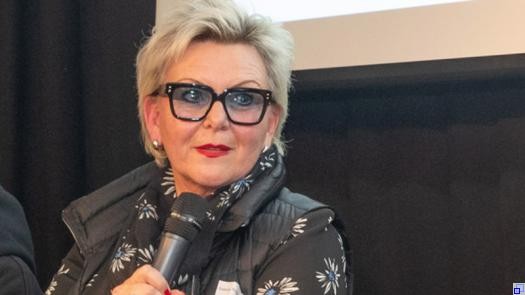 Porträtaufnahme von Frau Straub-Satzke. Sie trägt eine Brille, kurze blonde Haare, dunkle Kleidung und roten Lippenstift.