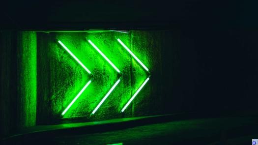 Grüne Neonröhren auf schwarzem Grund, die das FFWD-Zeichen zeigen.