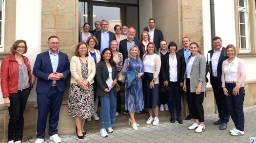 Eine Gruppe Menschen in Businesskleidung steht auf und vor den Stufen zum Eingang ins Plankstadter Rathaus.