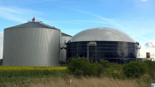 Biogasanlage auf einer Wiese, im Vordergrund ist ein Rapsfeld zu sehen.