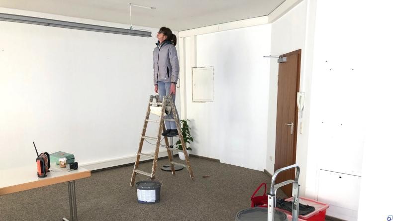 Bild: Stadt Eberbach Eine Frau steht auf einer Leiter und inspiziert eine Deckenleuchte. Um sie herum stehen Farbeimer und andere Renovierungsutensilien.