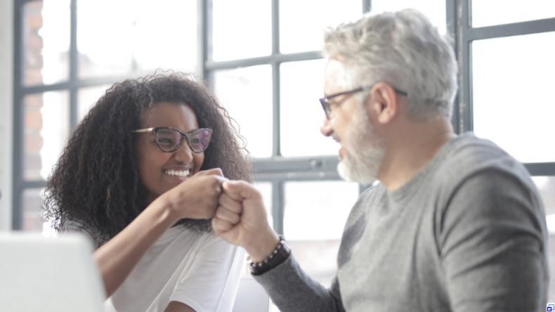 Bild: Pexels / Andrea Piacquadio Ein grauhaariger Mann mit Brille und eine junge Frau mit Brille sitzen vor einem Laptop und stoßen ihre Fäuste gegeneinander.