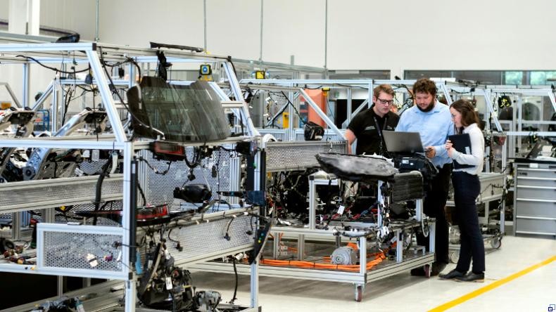 Bild: ThisisEngineering / Unsplash Drei Menschen stehen in einer Produktionshalle und betrachten einen Bildschirm, der an eine Maschine angeschlossen ist.