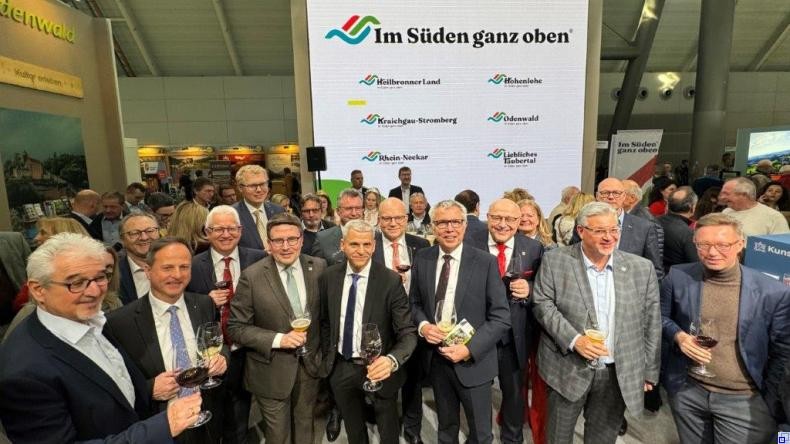 Foto: Tourimia Tourismus GmbH, Christoph Obel Mehrere Männer im Anzug stehen in einer Messehalle vor einer Werbewand mit dem Slogan "Im Süden ganz oben"