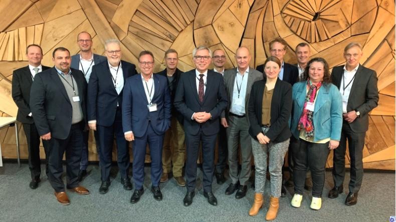 Bild: Rhein-Neckar-Kreis Landrat Stefan Dallinger steht mit den Teilnehmenden des Wirtschaftsdialogs vor einer hölzernen Wand. Bis auf zwei Anwesende ist der Kreis rein männlich besetzt.