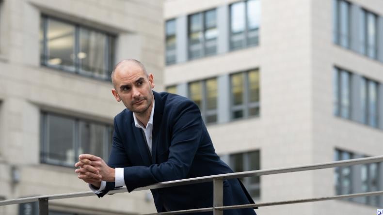 Bild: Ministerium für Finanzen Baden-Württemberg Dr. Danyal Bayaz lehnt vor einem Bürogebäudekomplex an einem Geländer und blickt nachdenklich zur Seite.