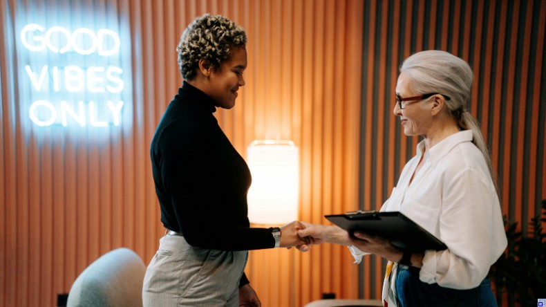 Bild: Unsplash Jüngere Frau und ältere Frau geben sich die Hand und lächeln sich an.