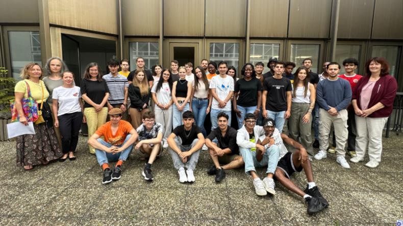 Bild: F+U Academy of Languages Eine Gruppe junger Menschen steht und sitzt, flankiert von mehreren Lehrkräften, vor einem Gebäude.