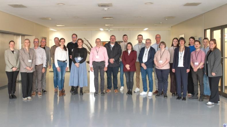 Bild: Rhein-Neckar-Kreis Eine Gruppe Menschen, weitgehend in Businesskleidung, steht in einem Innenraum. Alle lächeln.