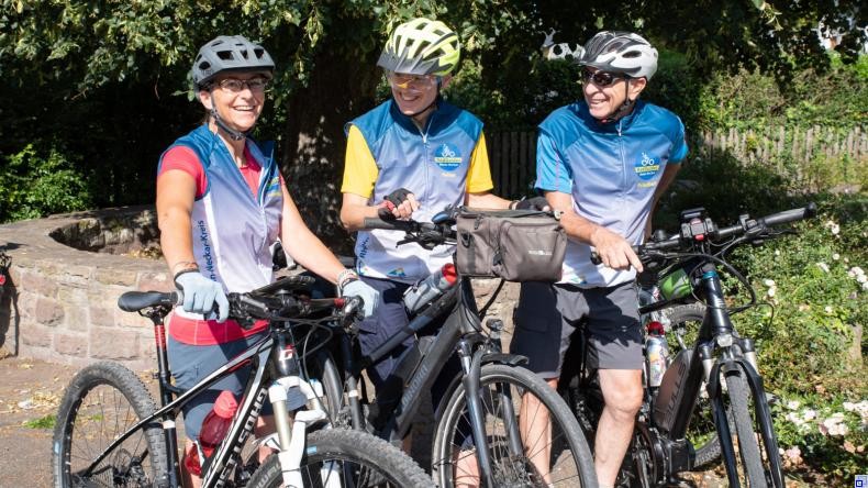 Bild: Rhein-Neckar-Kreis Drei Menschen mit Fahrrädern und RadGuides-Weste stehen beieinander und unterhalten sich lächelnd.