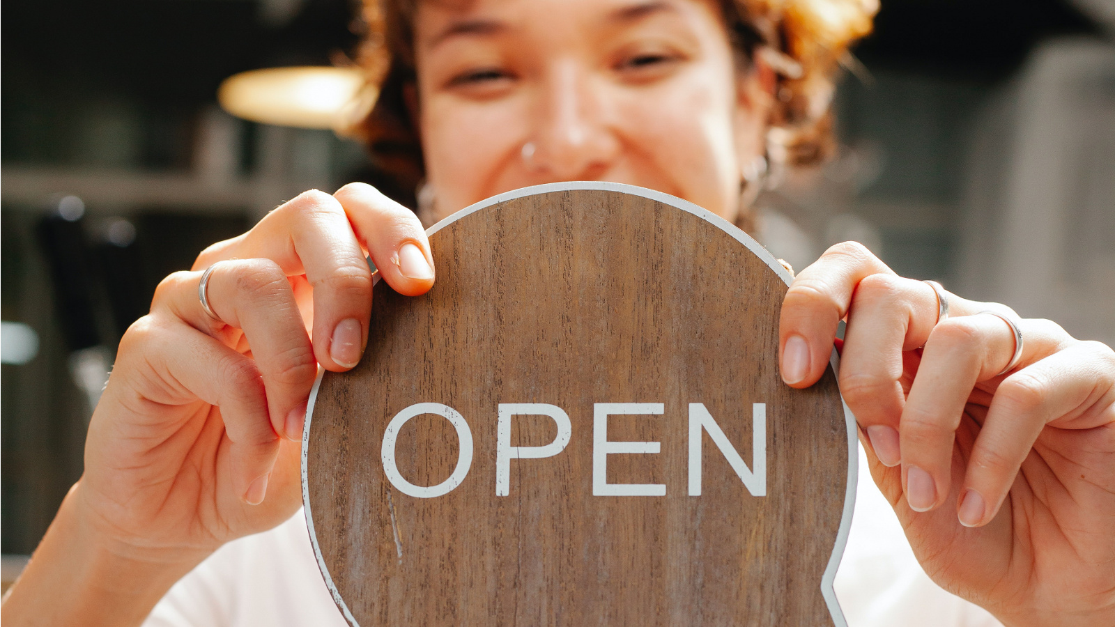 Glückliche Frau hält "Open"-Schild in die Kamera