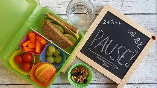 Foto einer Vesperdose mit Brot, Obst und Nüssen neben einer kleinen Schultafel mit der Aufschrift Pause