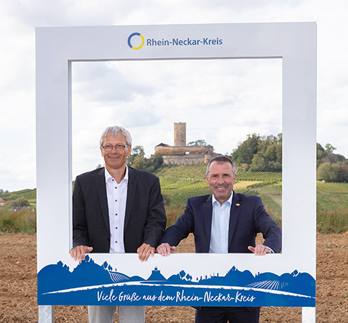 Landrat-Stellvertreter und Oberbürgermeister stehen im Fotorahmen, im Hintergrund ist die Burg Steinsberg zu sehen.