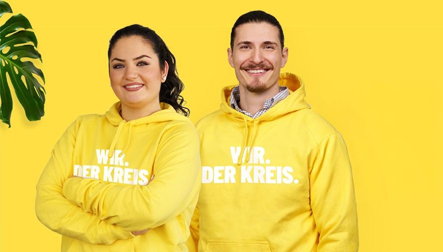 Mann und Frau tragen gelben "Wir der Kreis"-Hoodie