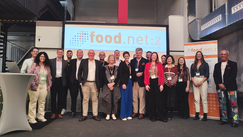 Eine Gruppe Menschen in Businesskleidung steht auf einer Bühne; im Hintergrund ist der Schriftzug food.net:z zu sehen.