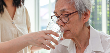 (Foto: Satkawat / stock.adobe.com) Pflegerin gibt älterer Frau ein Glas Wasser