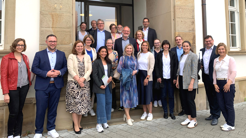 Eine Gruppe Menschen in Businesskleidung steht auf und vor den Stufen zum Eingang ins Plankstadter Rathaus.