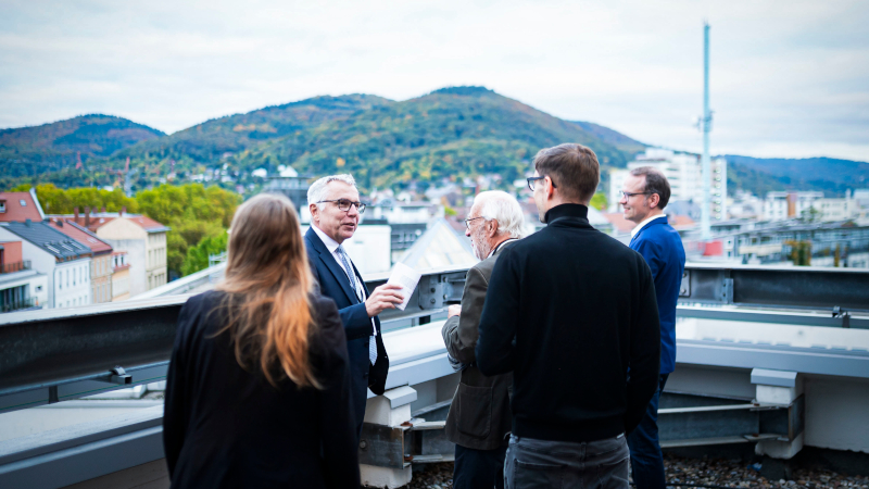 Landrat Dallinger und vier weitere Menschen stehen auf der Dachterrasse des Landratsamts; im Hintergrund ist die Stadt Heidelberg und der Odenwald zu sehen.