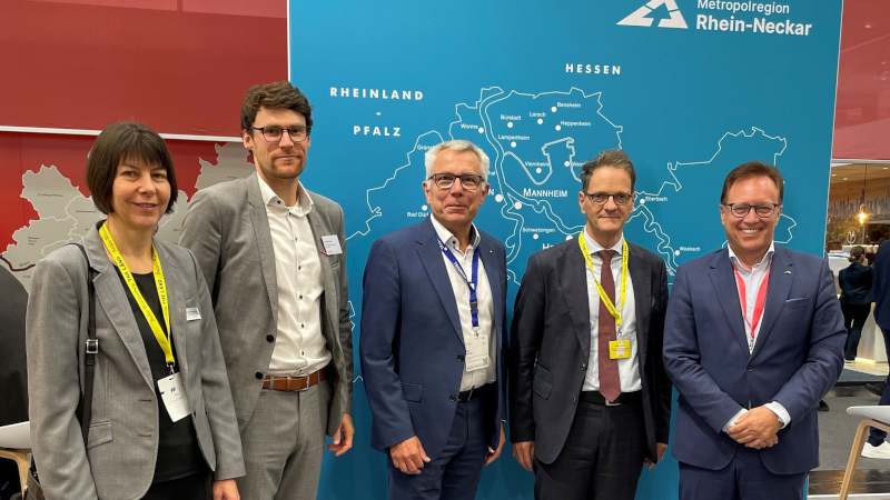 Eine Gruppe Menschen in Businessanzügen steht vor einer blauen Wand mit einer stilisierten Karte der Metropolregion.